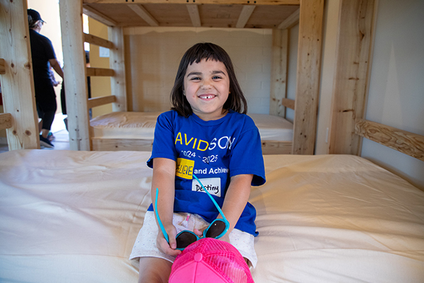 A girl in a blue t-shirt smiles on a bottom bunk